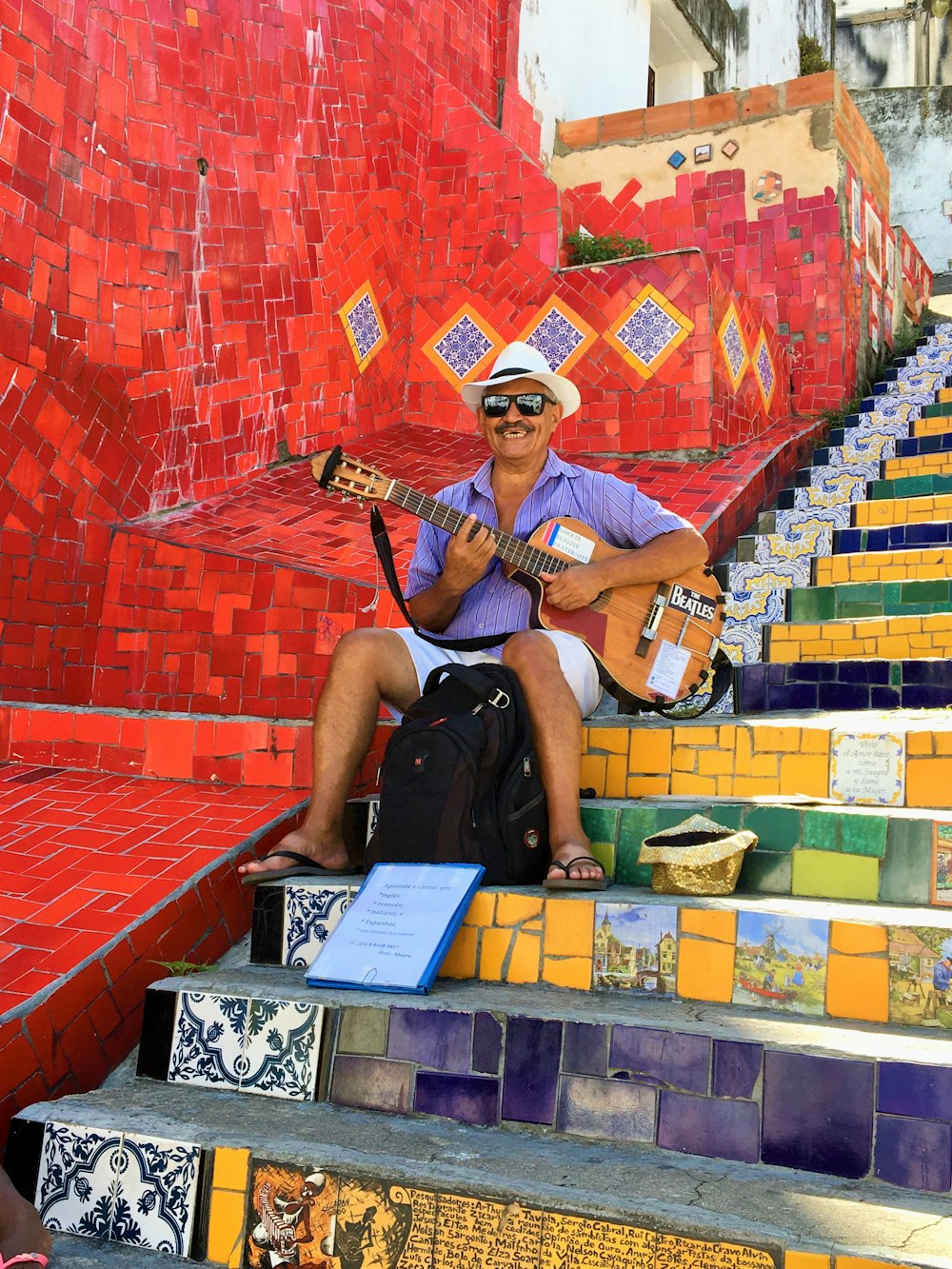 man in black shirt and brown pants sitting on yellow and red concrete stairs