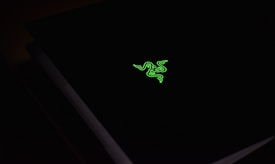 A dark surface with a vibrant green logo resembling three stylized snakes intertwined, illuminating against the black background.
