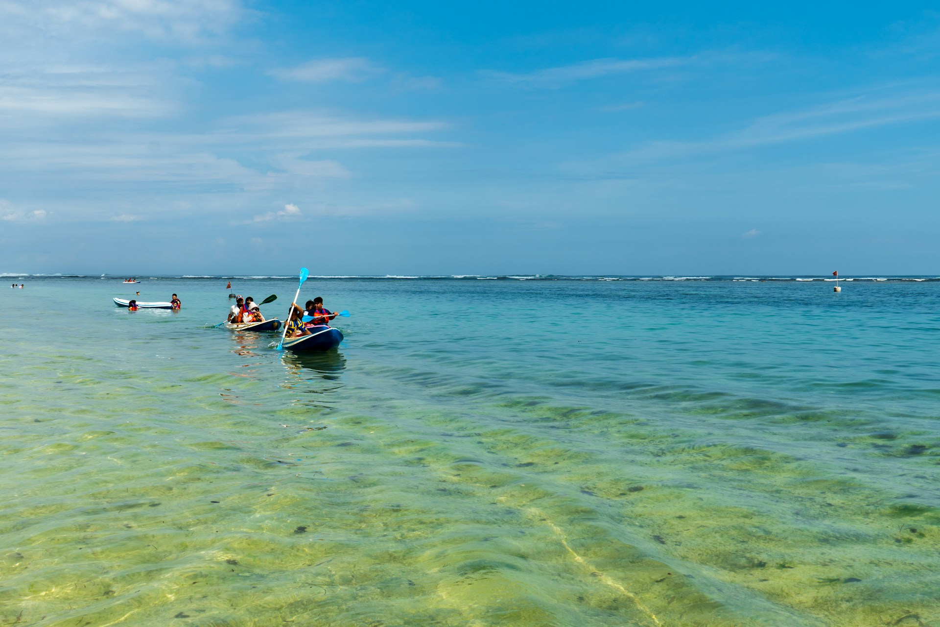 An adventurous group kayaking on crystal-clear blue waters under a bright sunny sky.