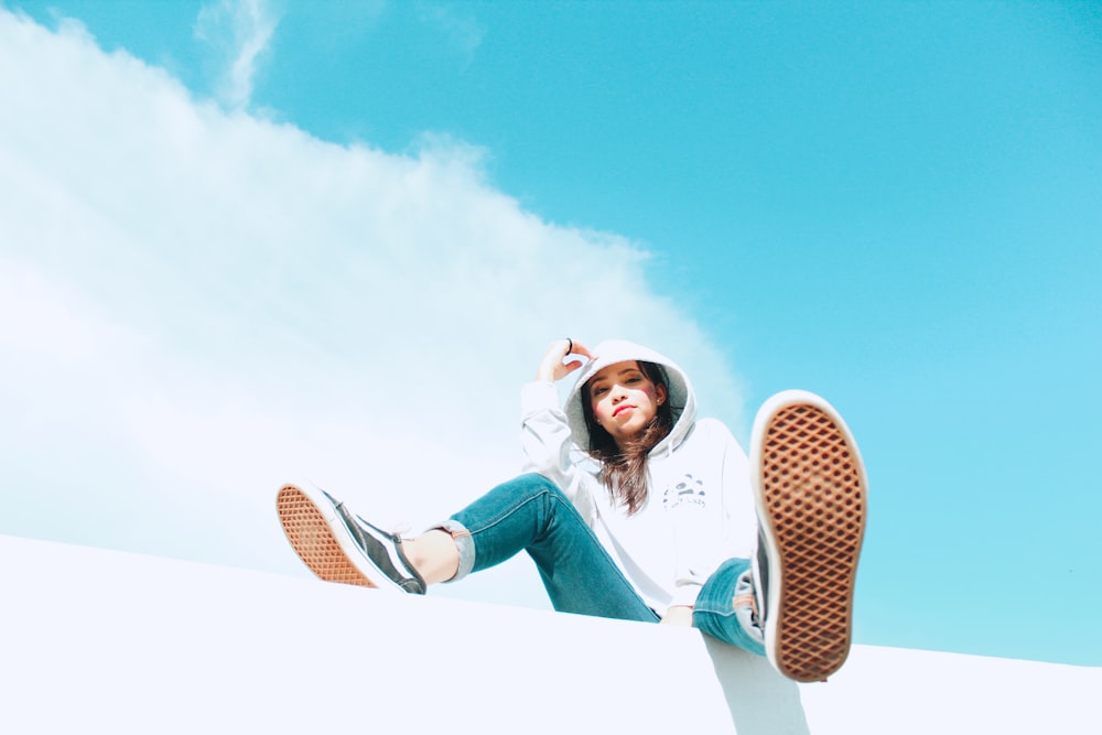 woman in blue denim jeans and white sneakers sitting on brown and white chair under blue