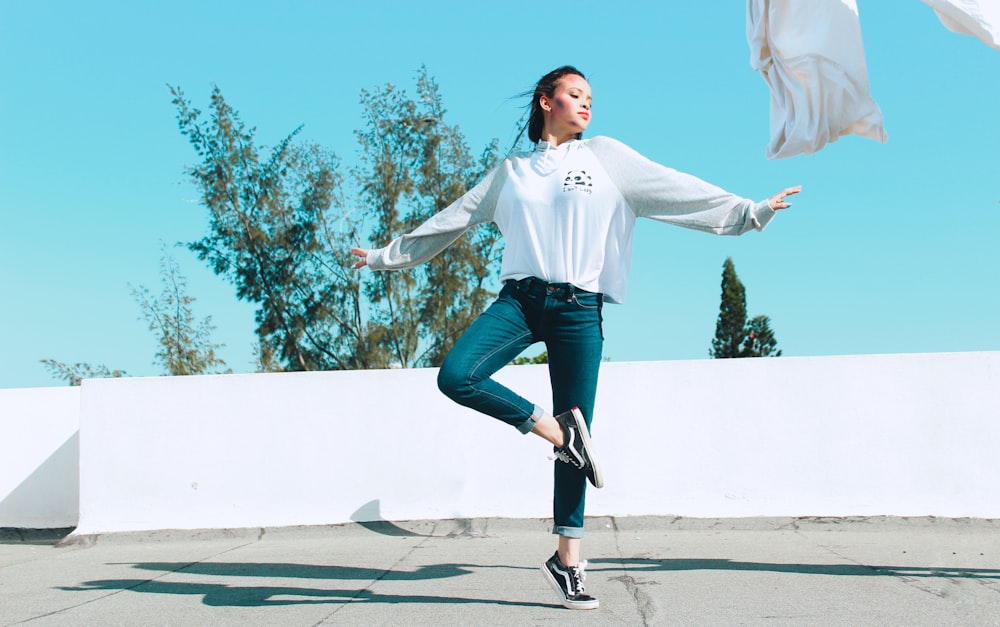 woman in white long sleeve shirt and blue denim jeans jumping on gray concrete road during