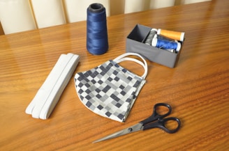 black handled scissors beside blue thread and white and black checkered pouch