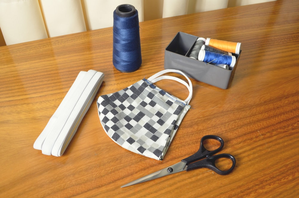 black handled scissors beside blue thread and white and black checkered pouch