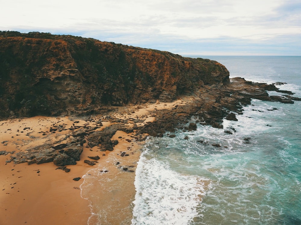 brown rocky mountain beside sea during daytime