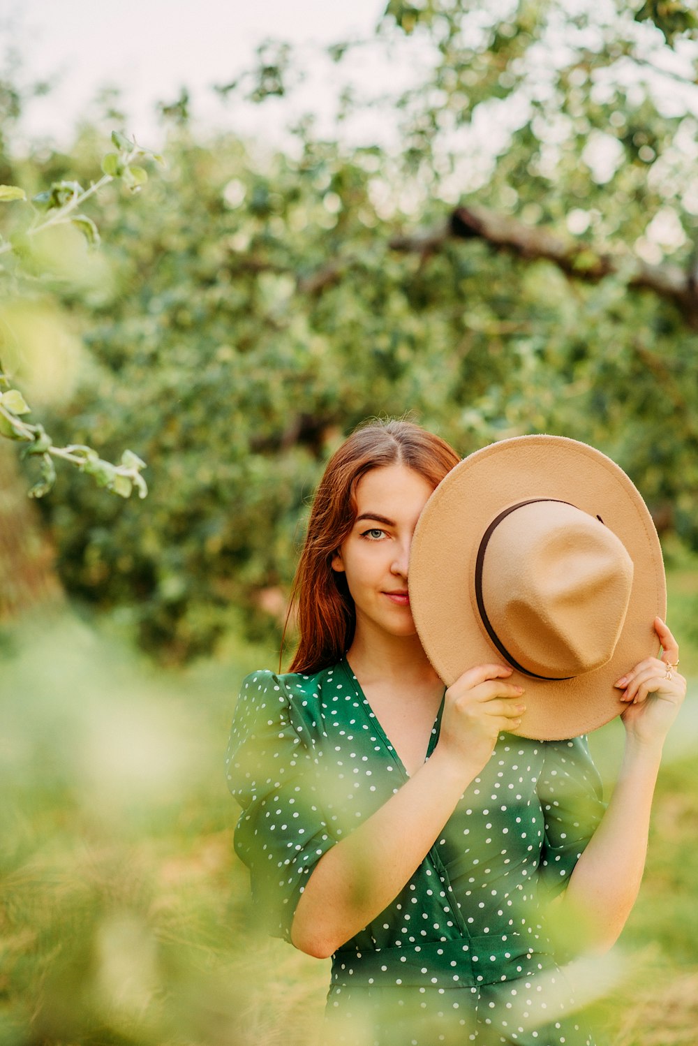 woman in green and white polka dot dress holding brown hat