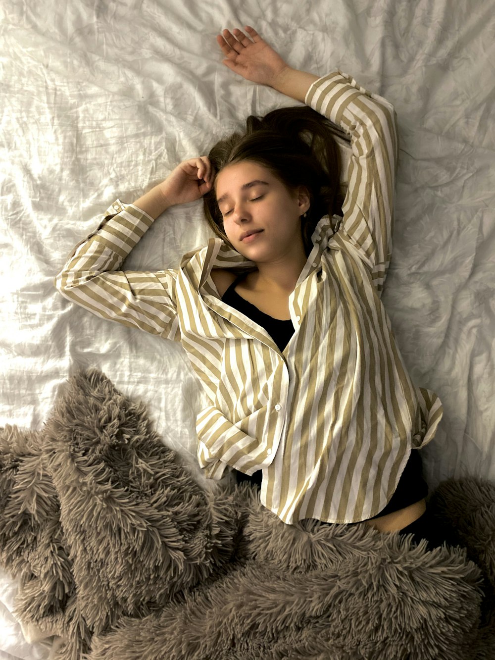 Frau in weiß und schwarz gestreiftem Langarmhemd liegt auf dem Bett