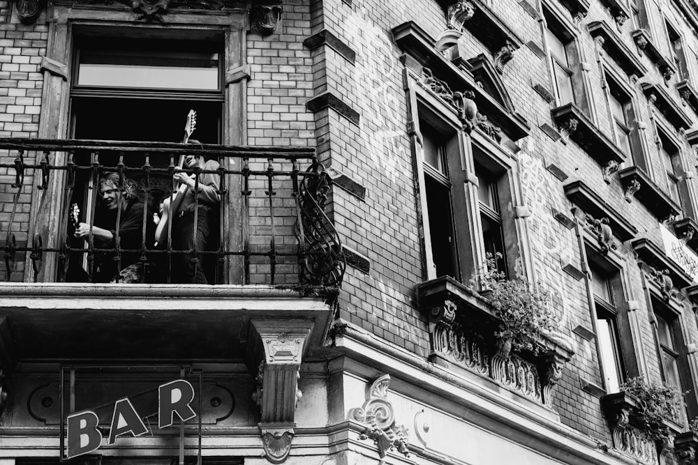 grayscale photo of man and woman standing on window