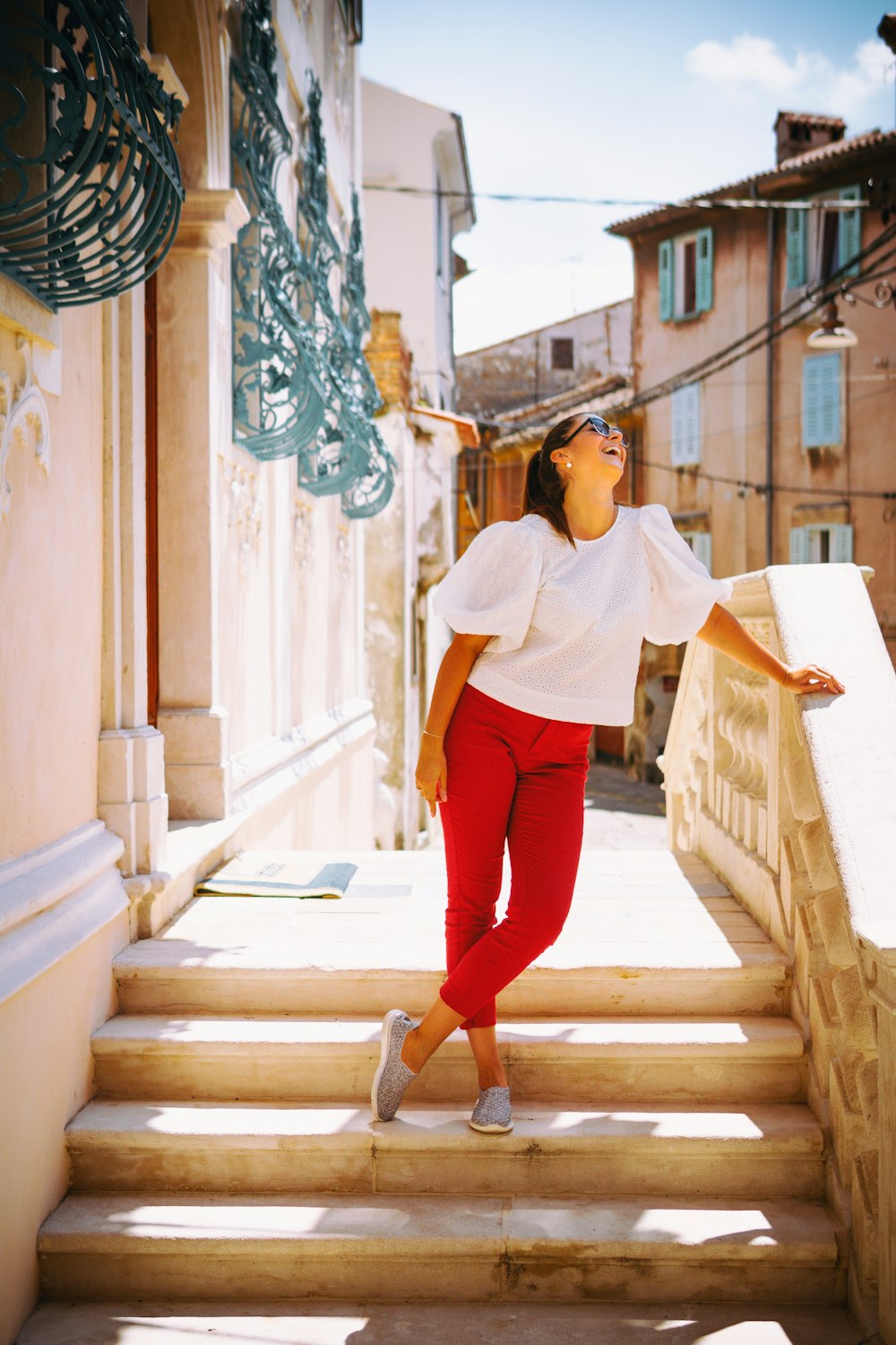mulher na camisa branca de manga comprida e calças vermelhas em pé nas escadas