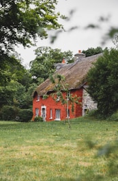 brown and white house near green trees under white clouds during daytime