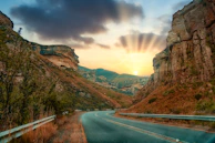A panoramic view of a winding highway cutting through rugged terrain at sunset.