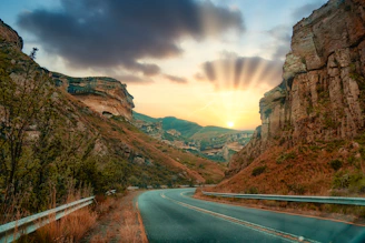 A panoramic view of a winding highway cutting through rugged terrain at sunset.