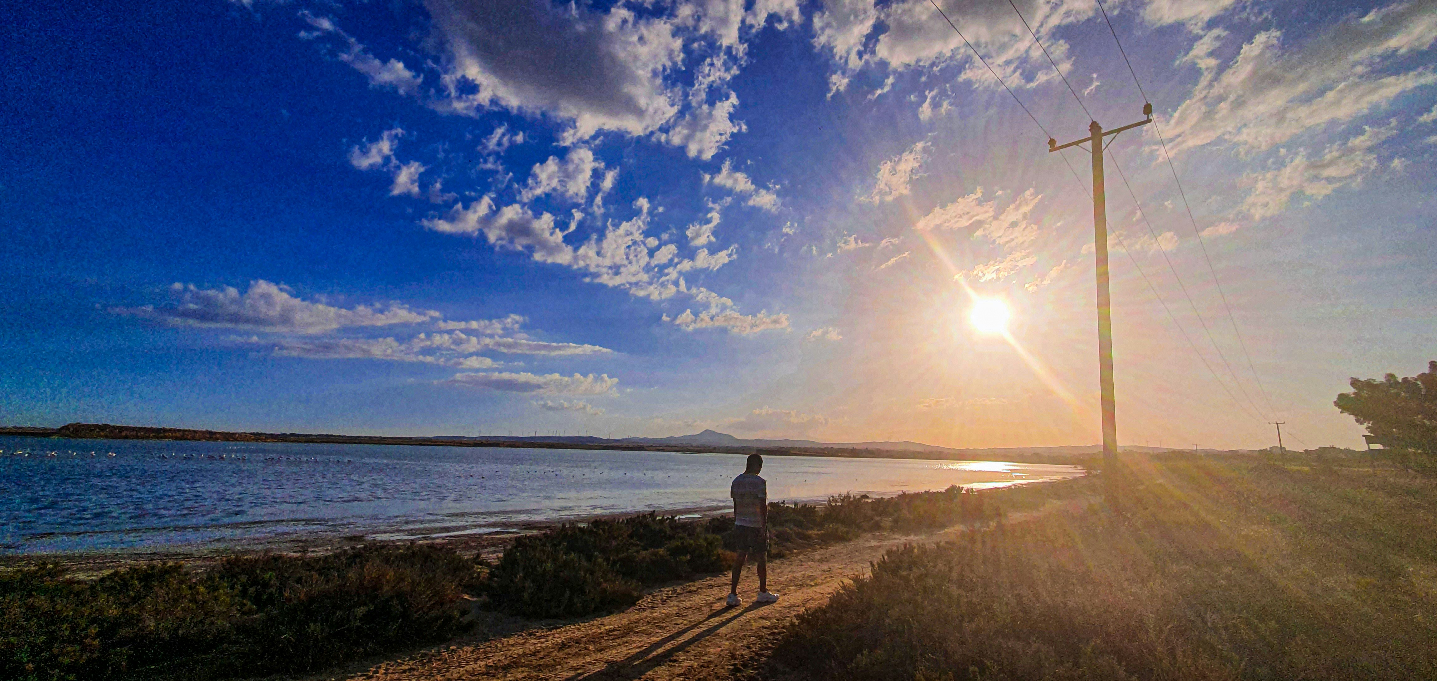 pessoa em pé na grama marrom perto do corpo de água durante o dia