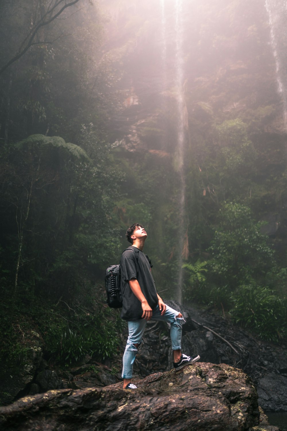 man in black jacket and blue denim jeans walking on pathway between green trees during daytime