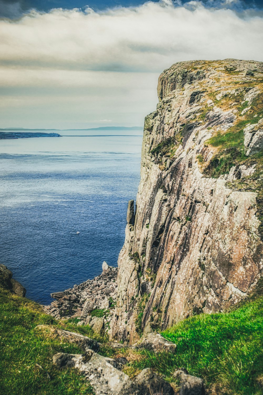 brown and green rock formation near blue sea under white clouds during daytime