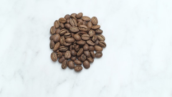 A pile of roasted coffee beans scattered on a smooth, light-colored surface.