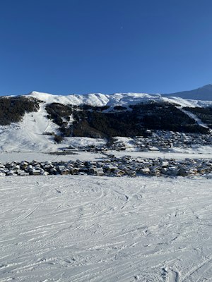 Aerial view of snow-covered Livigno village strung along its flat valley floor with pistes and lift lines on the wooded slope above