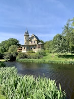 brown and white concrete building near green trees and river under blue sky during daytime