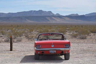 A convertible cruising along a desert highway with red rock formations.