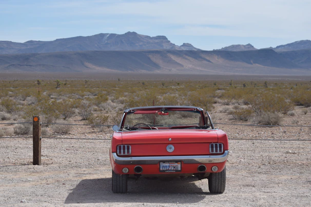 A convertible cruising along a desert highway with red rock formations.