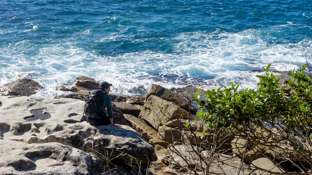 man in black jacket sitting on rock near body of water during daytime