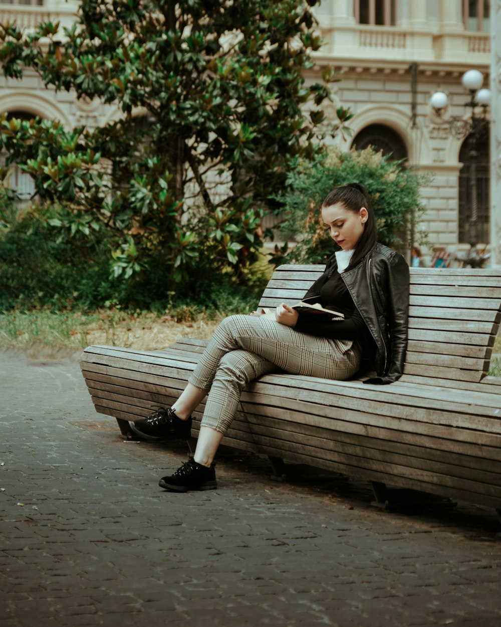 woman in black jacket and gray pants sitting on brown wooden bench