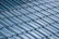 A close-up view of a roof with glossy, blue ceramic tiles arranged in a uniform, overlapping pattern. The tiles have a curved design and the surface reflects light, creating a shiny appearance.