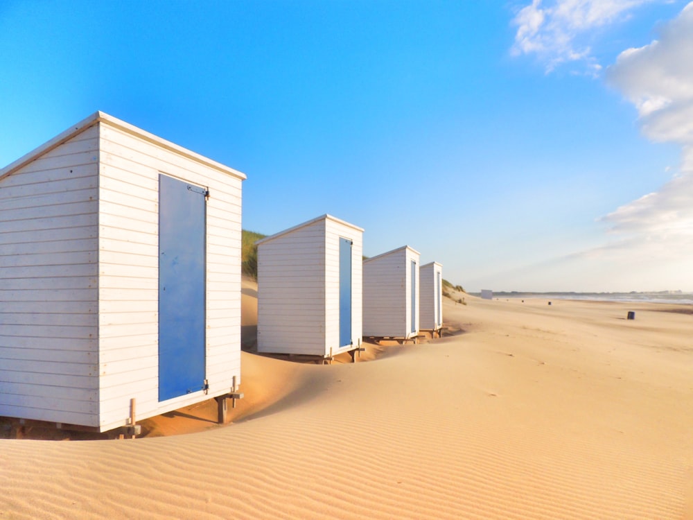 white wooden house on brown sand under blue sky during daytime