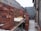 Stacks of red bricks are neatly arranged in a partially constructed building area. The walls are in various stages of construction, with some surfaces covered in unfinished plaster. There are tables holding bricks in preparation for further building work.