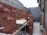Stacks of red bricks are neatly arranged in a partially constructed building area. The walls are in various stages of construction, with some surfaces covered in unfinished plaster. There are tables holding bricks in preparation for further building work.