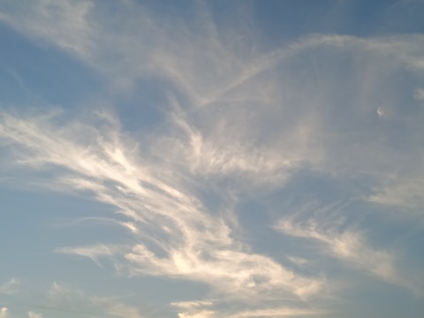 Light clouds are scattered across a clear blue sky. The clouds have a wispy texture and appear to be illuminated by the sunlight, giving a soft, serene appearance.