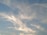 Light clouds are scattered across a clear blue sky. The clouds have a wispy texture and appear to be illuminated by the sunlight, giving a soft, serene appearance.