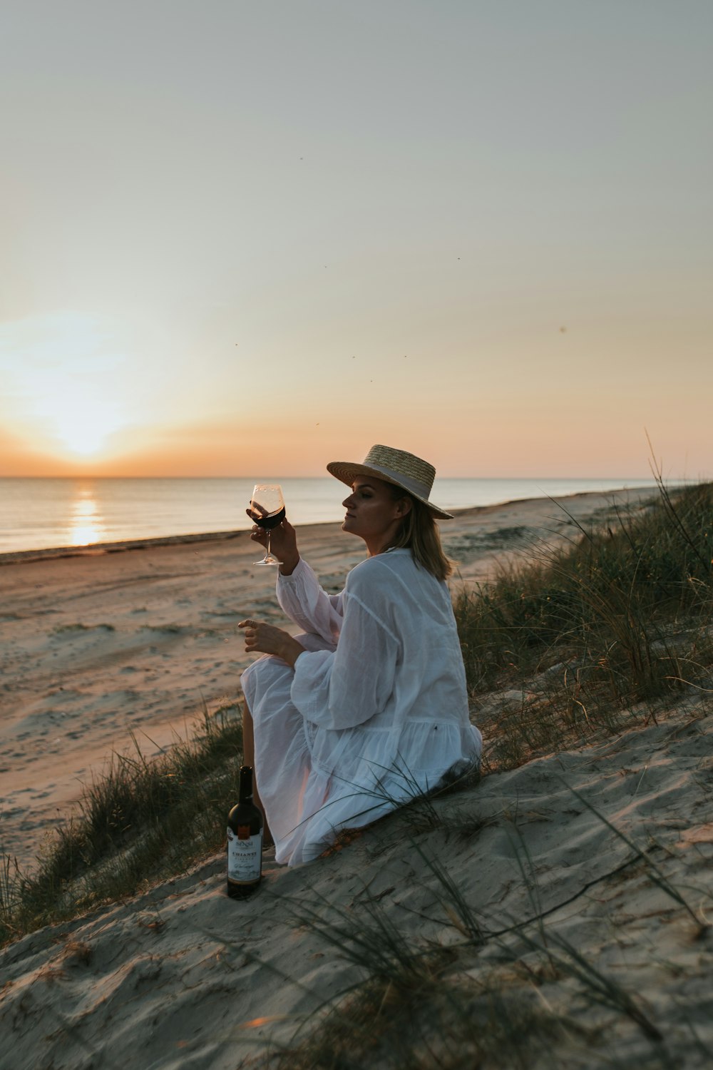 mulher na camisa branca de manga comprida e calças cinzas sentadas na rocha cinza perto do mar durante