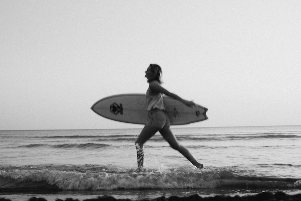 Photo en niveaux de gris d’une femme tenant une planche de surf sur la plage