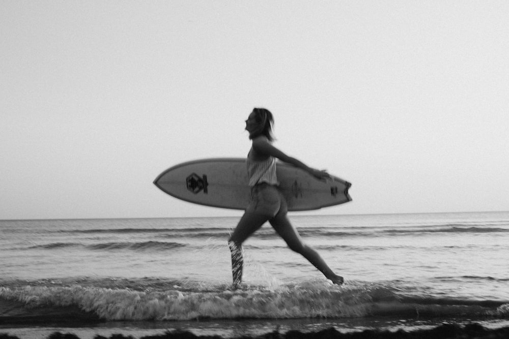 grayscale photo of woman holding surfboard on beach