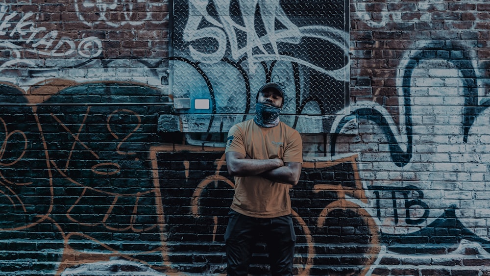 man in gray crew neck t-shirt and black pants standing beside wall with graffiti