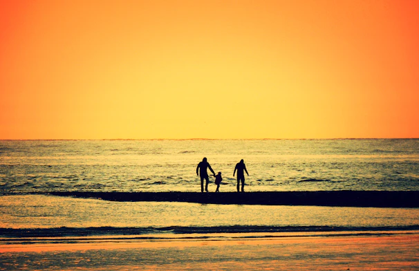 A warm sunset silhouette of a family walking hand in hand along the beach.