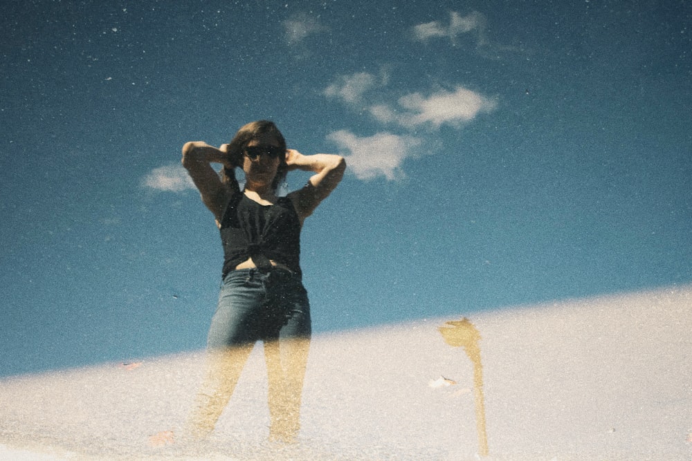 woman in black tank top and blue denim jeans standing on white sand under blue sky