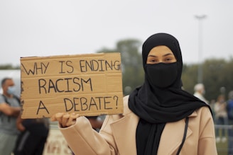 woman in black hijab holding brown wooden welcome to the beach signage