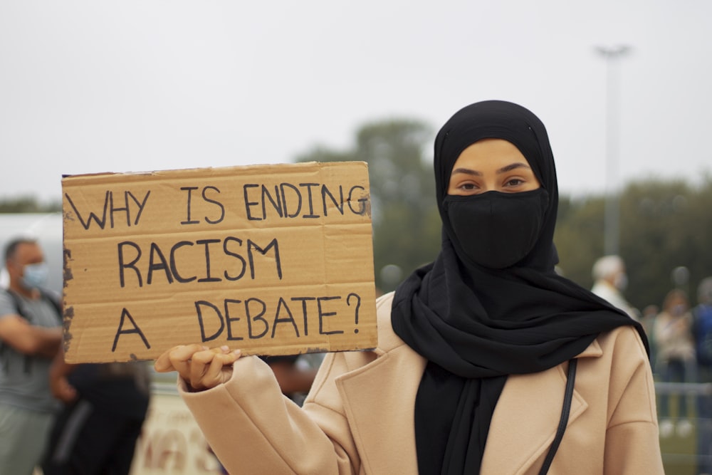 woman in black hijab holding brown wooden welcome to the beach signage