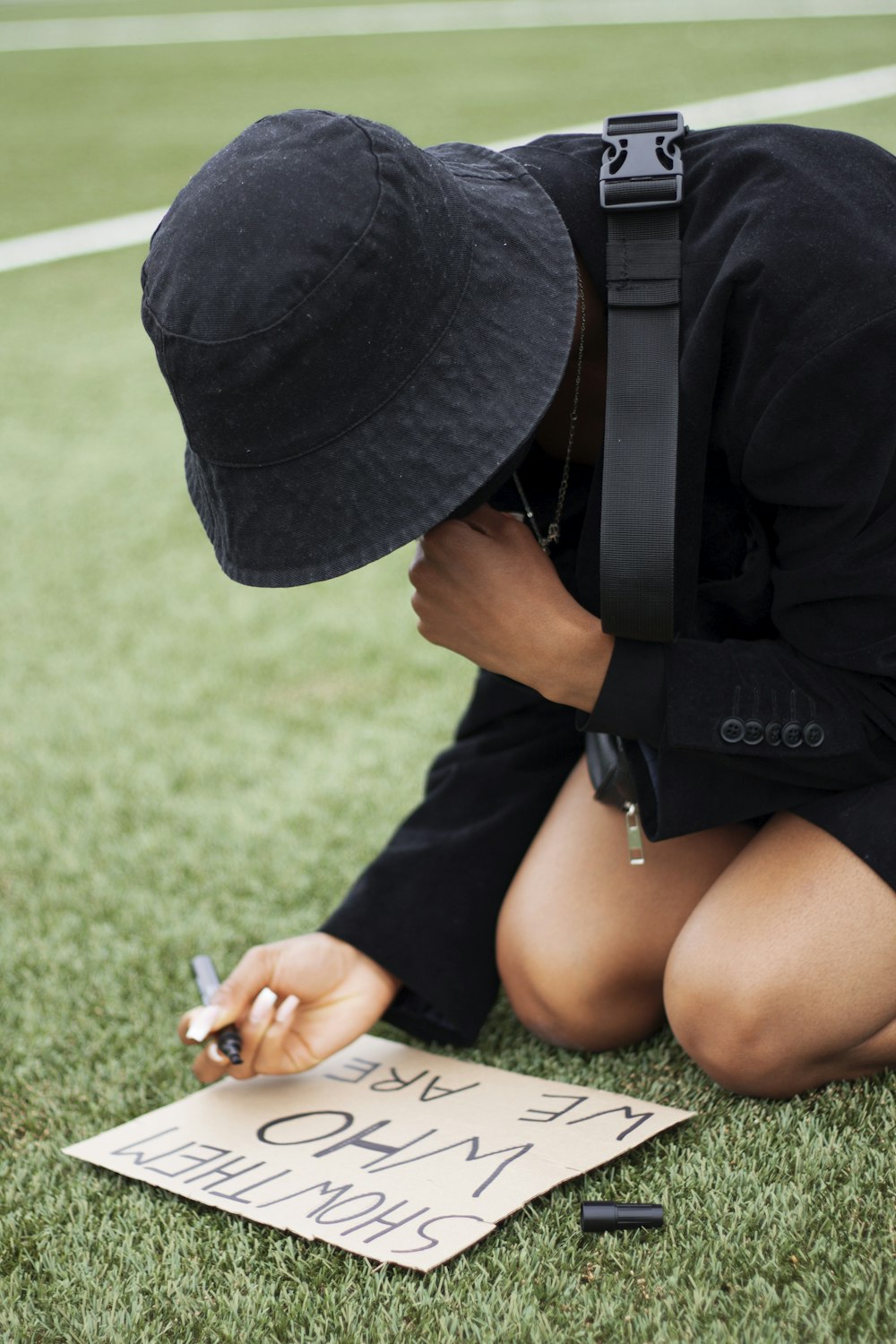woman in black hat and black t-shirt sitting on green grass field during daytime