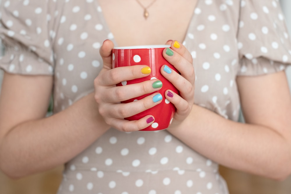 woman in white and black polka dot dress holding red and white polka dot ceramic mug