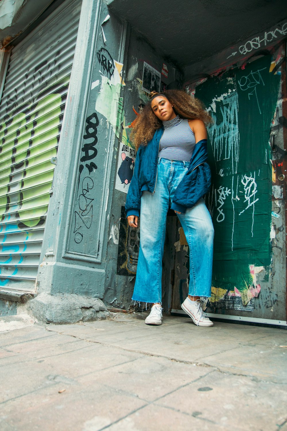 woman in blue denim jeans and white sneakers standing beside green and white wall