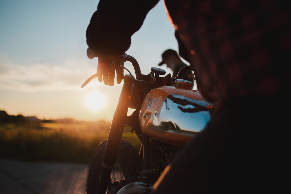 man in black and red checkered dress shirt riding on orange motorcycle during sunset