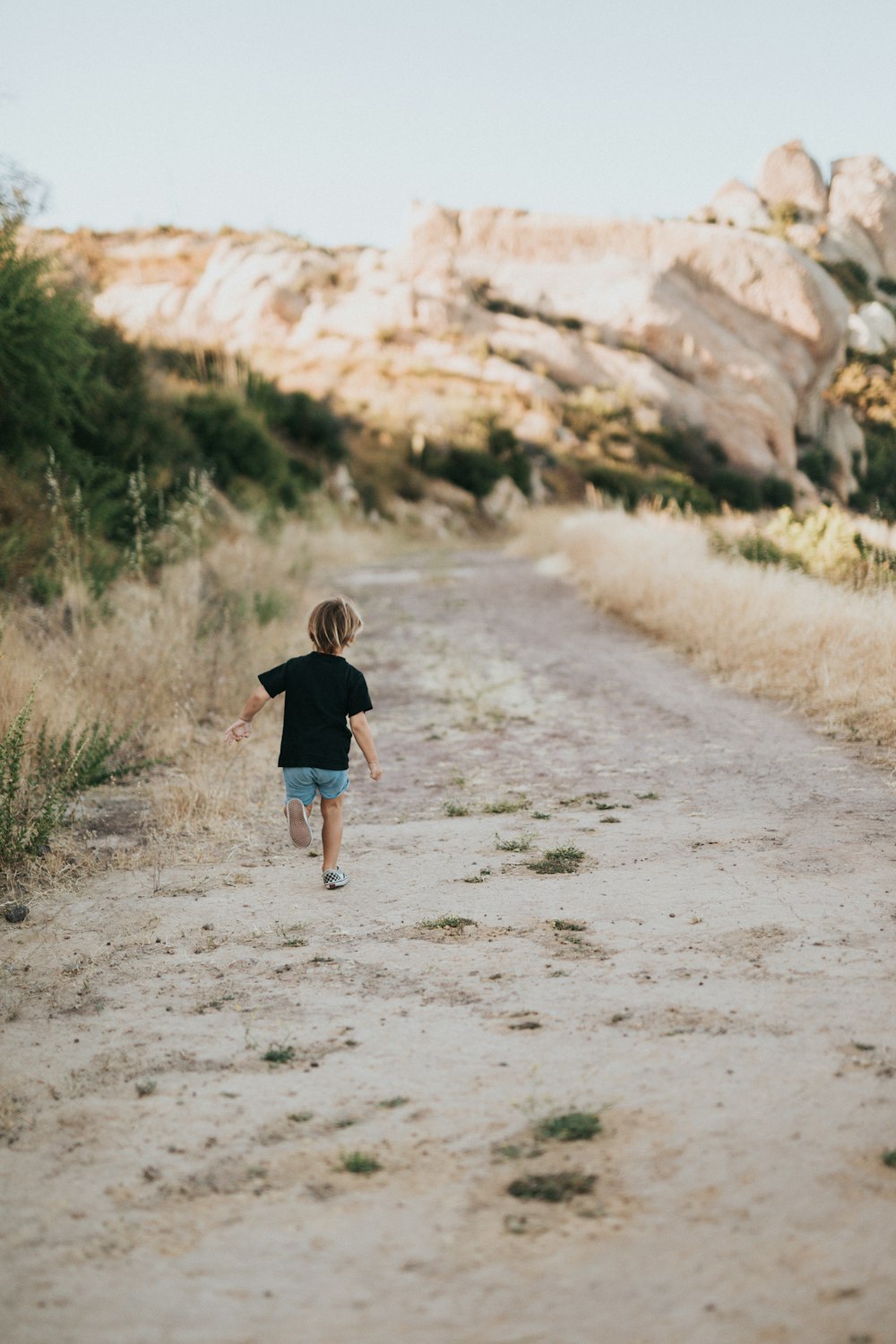 girl in black shirt walking on dirt road during daytime