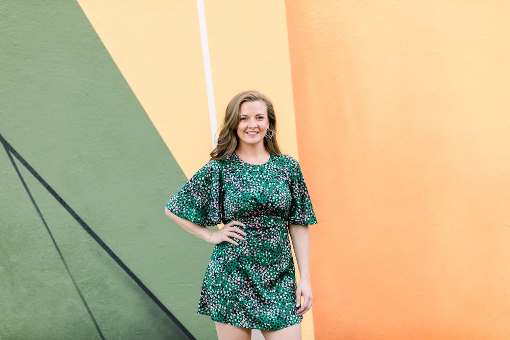 woman in black and white floral dress standing beside green wall