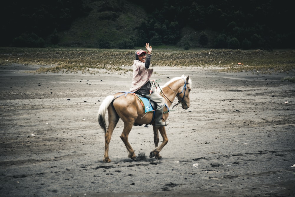 man in white shirt riding brown horse on gray sand during daytime