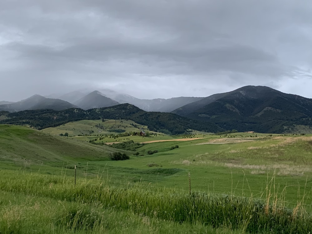 green grass field near mountain under white clouds during daytime