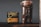 A clear glass jar filled with roasted coffee beans is placed next to a black package of Onyx Coffee Lab's Ethiopia Agaro Family coffee. The package contains detailed information about the coffee, including its origin and flavor notes. The background is a plain, gray wall, and the items are positioned on a dark wooden surface.