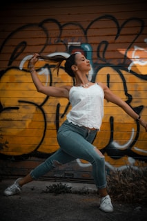 woman in white tank top and blue denim jeans sitting on brown wooden log