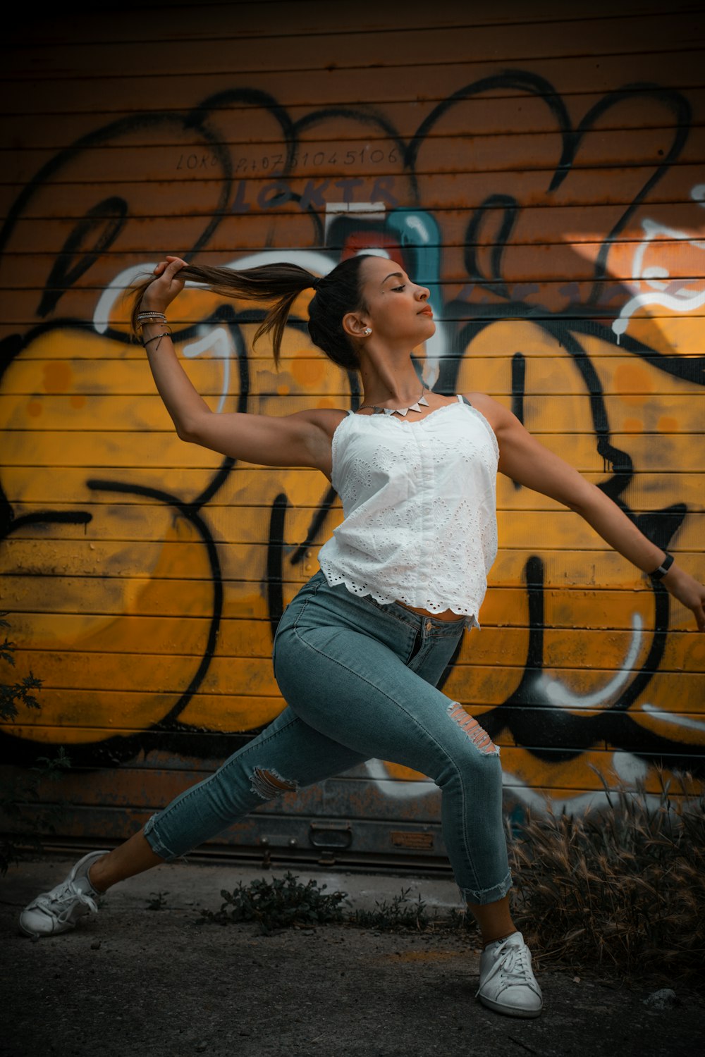 woman in white tank top and blue denim jeans sitting on brown wooden log